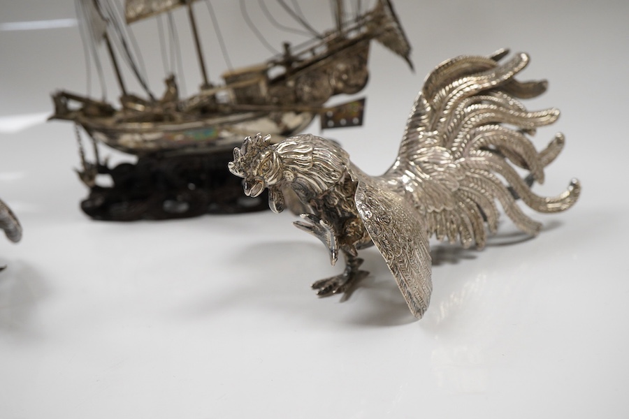 A pair of modern silver fighting cocks, import marks for Sheffield, Assay Office, Sheffield, 1977, height 68mm, together with a Chinese white metal miniature model of a ship, on a carved hardwood base, overall height 20.